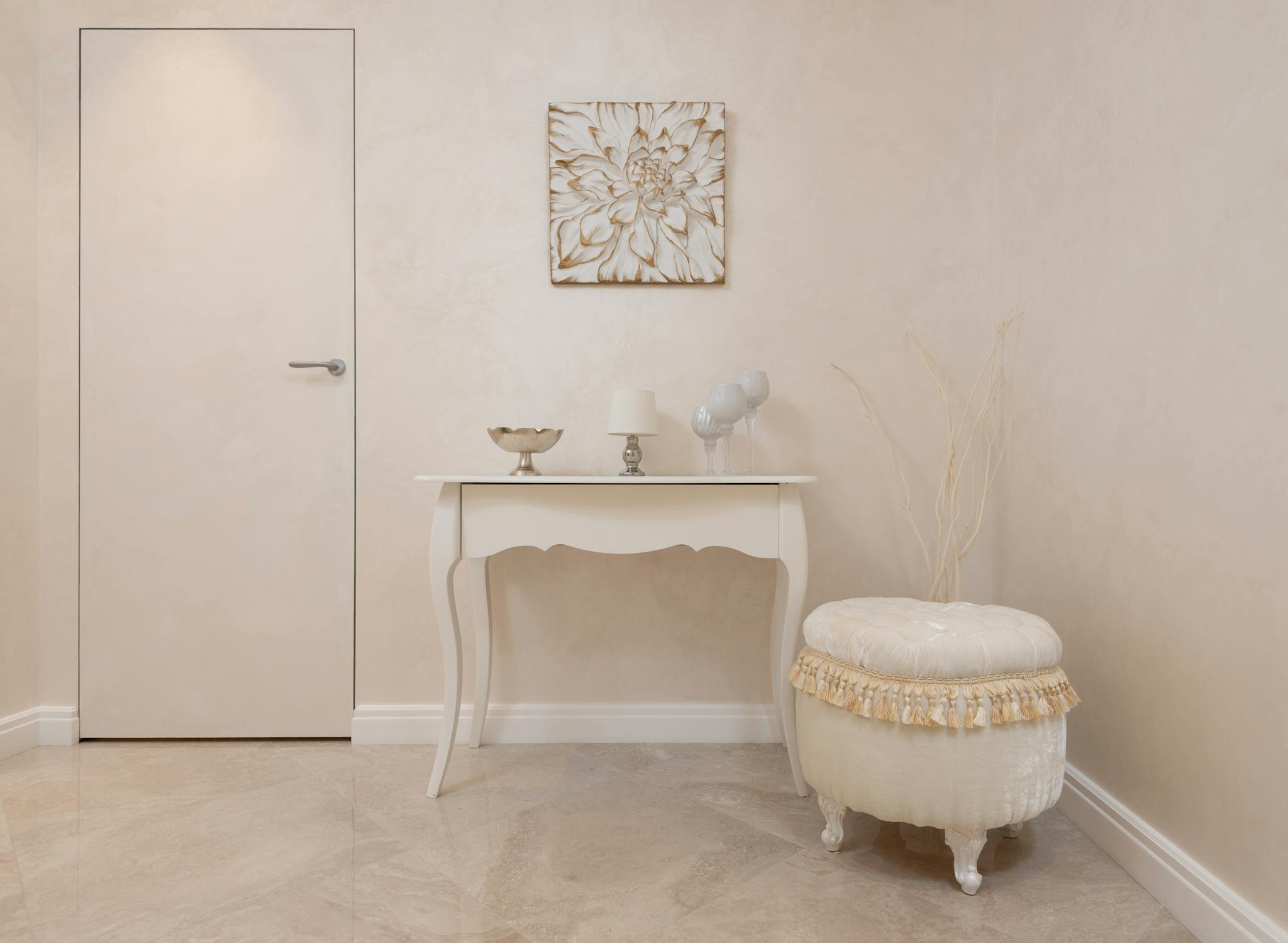 Interior of neutral colored entrance with beige walls and laminate furnished with table and soft pouf
